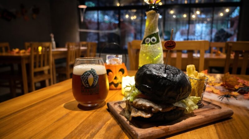 Hambúrguer com pão preto, cerveja artesanal e decoração temática de Halloween na Cervejaria Manube, em Santos.
